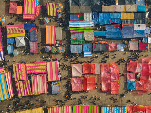 Aerial view of a vibrant outdoor market in Bogura, featuring colorful fabric canopies, stalls, and people walking through the crowded aisles in Bogura, Rajshahi Division, Bangladesh.
