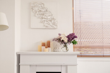 Obraz premium Flowers in vase and candles on fireplace in interior of stylish living room