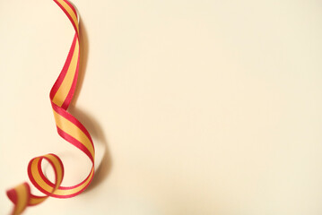 Spanish flag colored ribbon on beige background in a design with copy space. Concept: celebration of national holidays or national achievements.