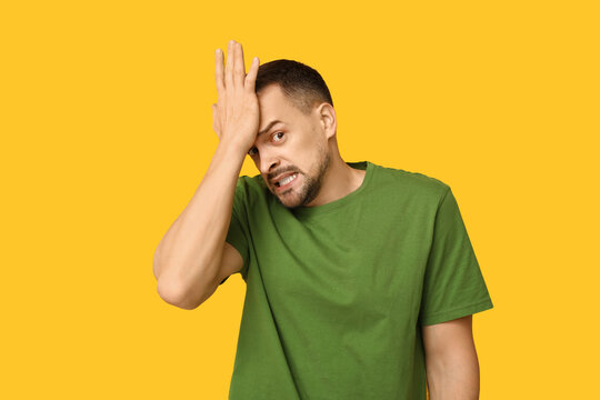 Handsome ashamed young man covering face with hand on yellow background