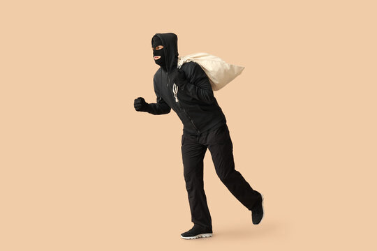 Male thief with bag on beige background