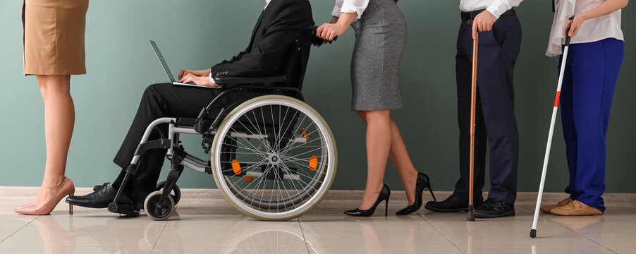 Job applicants with sticks and man in wheelchair waiting for interview near green wall