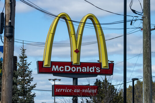 Quebec, Canada, 24 April 2026 : A McDonald's restaurant sign featuring Golden Arches and a Canadian maple leaf stands against a blue sky.