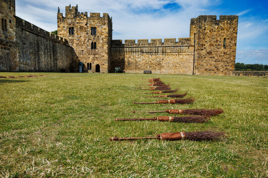 Line of broomsticks laid on grassy yard before historic castle