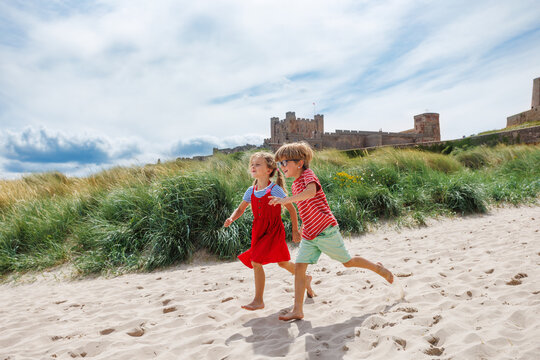 Children joyfully running on sandy beach near Bamburgh castle