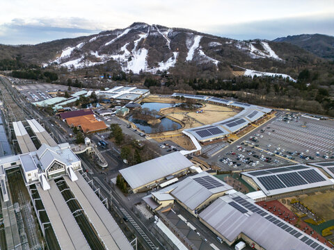 Aerial view of Karuizawa Prince Shopping Plaza with its distinctive buildings, parking lots, and ponds, set against the backdrop of snow-covered ski slopes in Karuizawa, Nagano, Japan.