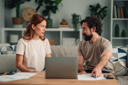Couple discussing financial problems at home, reviewing documents, dealing with money stress and large debt