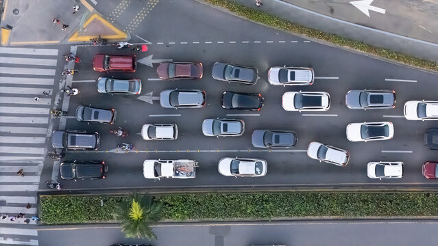Aerial view of a busy city intersection with multiple cars waiting at a crosswalk, including a white pickup truck, various sedans, and motorcycles, in the Dominican Republic.