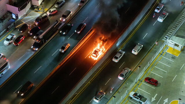 Aerial view of a burning car on a highway at night with flames and smoke rising from the vehicle amidst surrounding traffic in the Dominican Republic.