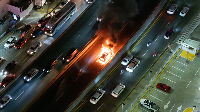 Aerial view of a car engulfed in flames on a busy highway at night with surrounding traffic and smoke rising in the Dominican Republic.