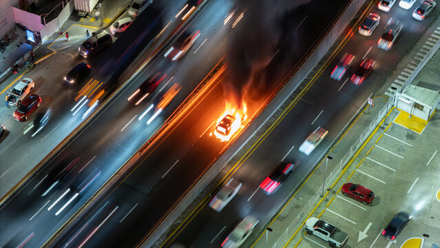 Aerial view of a car engulfed in flames on a highway at night with light trails from passing traffic in the Dominican Republic.