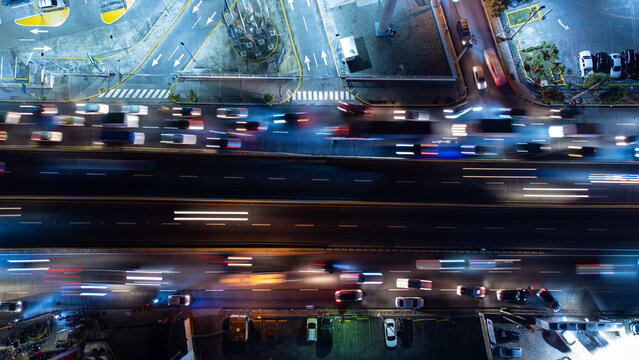 Aerial view of a busy highway at night with long exposure light trails from moving vehicles, illuminated road markings, and surrounding parking areas in the Dominican Republic.