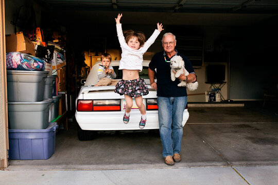 Girl Jumping off Car in Garage, with family