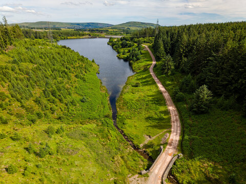 Aerial drone view of Carno Reservoir surrounded by lush green pine forests in Wales