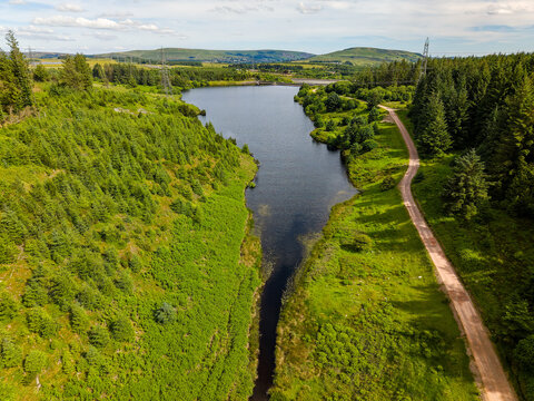 Aerial view of Carno Reservoir surrounded by green pine forests in Wales