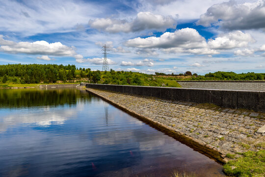 Stone dam wall bordering a calm water reservoir reflecting fluffy clouds
