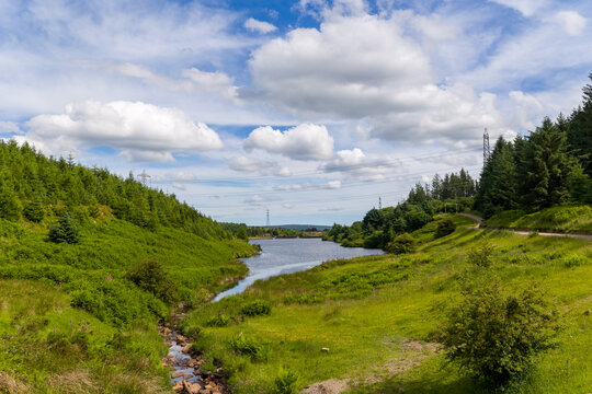 Beautiful rural valley with a flowing stream leading to a reservoir under white clouds
