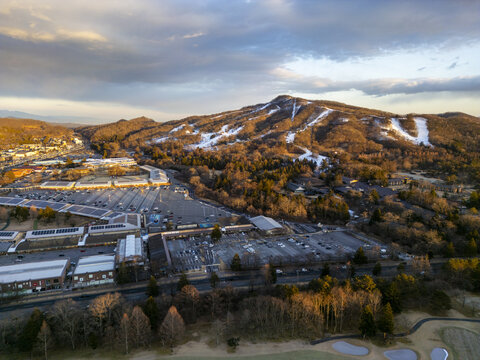Aerial view of Karuizawa Prince Shopping Plaza with parking lots and retail buildings at the base of a snow-dusted mountain under a golden sunset sky in Karuizawa, Nagano, Japan.