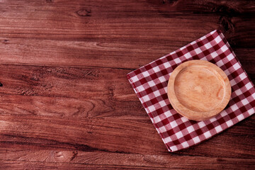 Fototapeta premium Wooden table holds a simple, warm-toned plate. Red and white checkered cloth adds cozy charm. Background features clean, paneled walls. Perfect for cafe, kitchen, or rustic lifestyle scenes