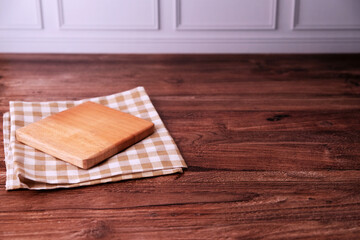 Fototapeta premium Square wooden board rests on checkered cloth. Wood grain shows warm, natural texture. Dark wood table provides rustic backdrop. Simple, clean composition invites creativity
