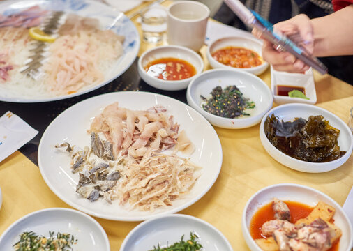 These images capture a diner using a smartphone to photograph a rich spread of Korean coastal delicacies, including sashimi and traditional banchan. It beautifully highlights modern digital dining cul
