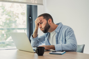 Naklejka premium Frustrated man feeling burnout and experiencing a headache while concentrating on his work at the computer screen, reflecting stress and exhaustion from a demanding day in the office