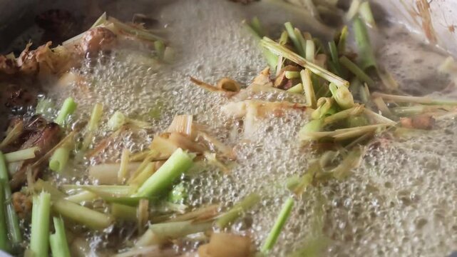 Close up footage of boiling water with fresh lemongrass, ginger and herbal ingredients, bubbling in a pot for healthy traditional soup or organic medicinal infusion clip
