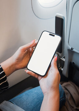 Person traveling by air holding a modern mobile phone with a customizable white display, creating a space for applications or travel content in the aircraft cabin