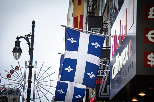 MONTREAL, CANADA - DECEMBER 23, 2016: Quebec flags hang in front of Montreal storefronts, business activity, shops. Also known as Fleur de Lys, or fleurdelise, it is the symbol of province of Quebec.