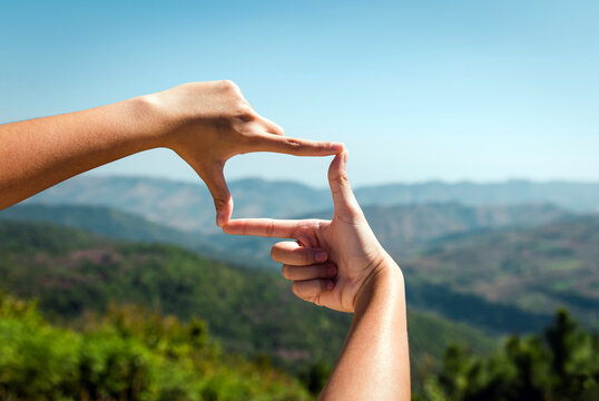 hand with a frame. hand framing view distant over sunset on mountain. Two hands cupped together, framing the vibrant golden sun setting over a distant mountain range, with dramatic clouds filling.