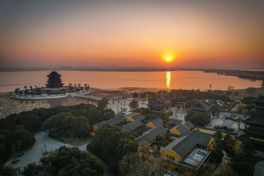 Aerial view of Chongyuan Temple at sunset, featuring traditional Chinese architecture, pagodas, and lush trees situated by the calm waters of Yangcheng Lake in Suzhou, Jiangsu, China.