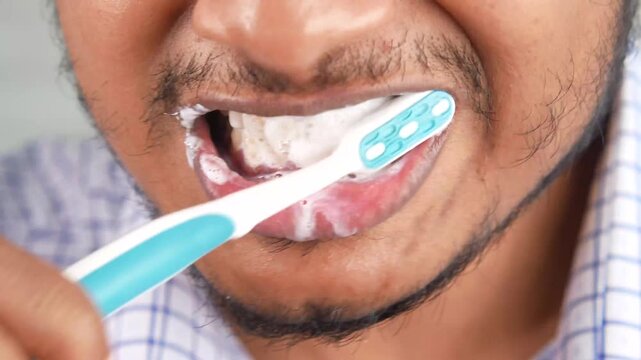 Close up of man brushing teeth with white toothpaste and blue toothbrush in morning bathroom routine