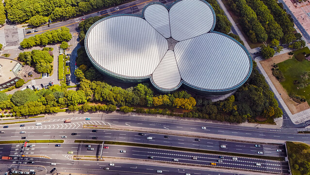 Aerial view of the Shanghai Oriental Art Center with its distinctive petal-shaped roof surrounded by lush green trees and a busy multi-lane highway in Shanghai, Shanghai, China.
