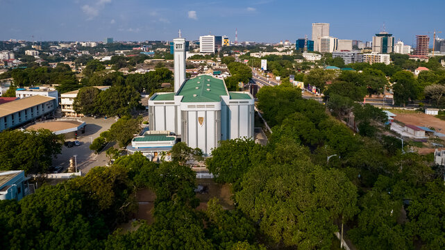 Aerial view of the Holy Spirit Cathedral surrounded by lush green trees and urban buildings under a clear blue sky in Accra, Greater Accra Region, Ghana.