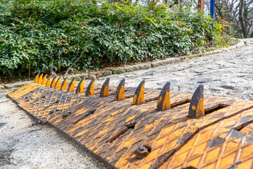 Obraz premium Orange and black anti-vehicle spike security strip installed on a road surface with green hedge behind, urban access control infrastructure.