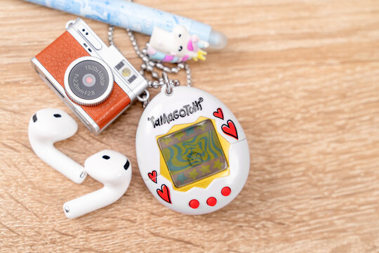 Bar, Montenegro: February 6, 2026: Retro Tamagotchi keychain, miniature camera and white wireless earbud on a wooden table, fun tech accessories flatlay concept.