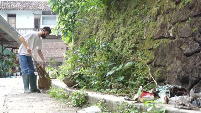 Middle portion of clip shows a man in a white shirt and jeans sweeping a cracked concrete path beside a mossy wall in an outdoor residential setting