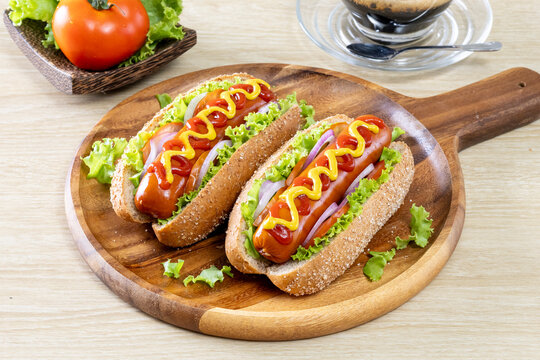 Two hot dogs topped with mustard and ketchup, along with various vegetables, are placed on a wooden platter.