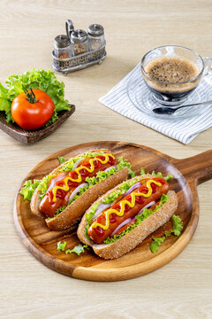 Two hot dogs topped with mustard and ketchup, along with various vegetables, are placed on a wooden platter.