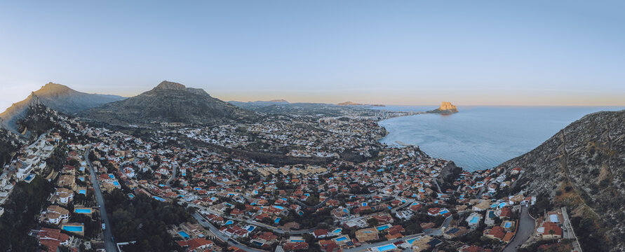 Aerial view of the coastal town of Calp featuring the Penon de Ifach, residential areas with red-tiled roofs, and the Mediterranean coastline at sunset, Calp, Valencian Community, Spain.