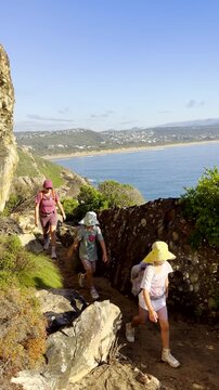 Mom and twin daughters on Robberg coastal hike with seascape views. Vertical