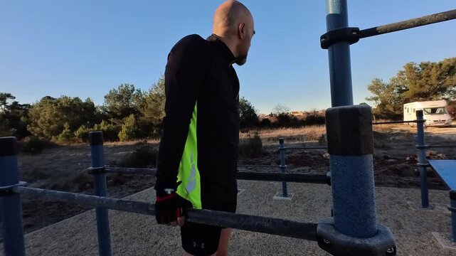 A detailed shot of an athletic man doing dips on parallel bars in an outdoor fitness park during a sunny morning.
The clip focuses on the effort and form of the exercise.