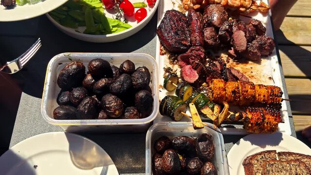Assorted grilled foods and vegetables served outdoors during shared meal, potatoes zucchini fresh cherry tomatoes and salad for picnic