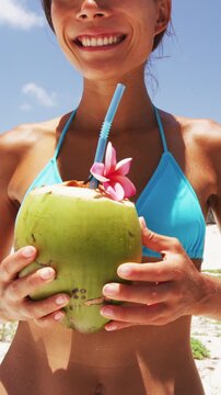 Bikini girl drinking healthy coconut water for weight loss on tropical beach vacation. Cute woman sipping from a straw in on Caribbean destination. Video is unretouched and model without makeup.