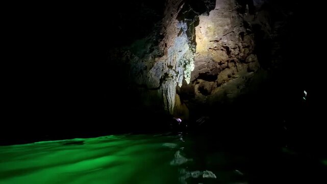 Swimmers explore a dark cave with illuminated green water and rocky walls at night