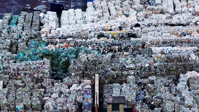 Aerial close abstract texture view of stacked recyclable waste bales at processing facility, drone tracking left