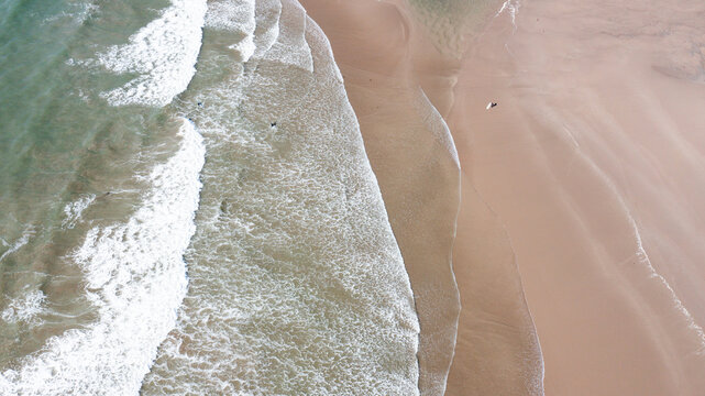 Aerial view of Bantham Beach with waves crashing on the sandy shore and surfers in the water in Kingsbridge, Devon, United Kingdom.