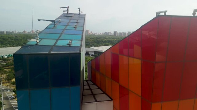 Aerial rising reveal of colorful tile facade on Ventana al Mundo monument with Barranquilla skyline highway and mangroves in tropical Colombia