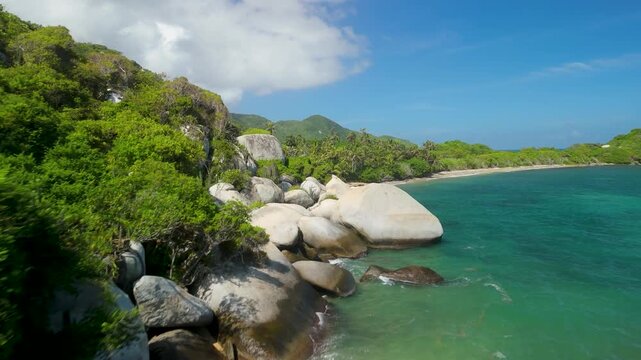Aerial forward flight over giant granite boulders and turquoise water along jungle coastline at Playa La Piscina in Parque Tayrona near Santa Marta Colombia