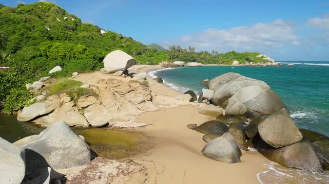 Aerial parallax above giant granite boulders on golden sandy beach with turquoise water and jungle hills at Playa Ca&ntilde;averal in Parque Tayrona near Santa Marta Colombia